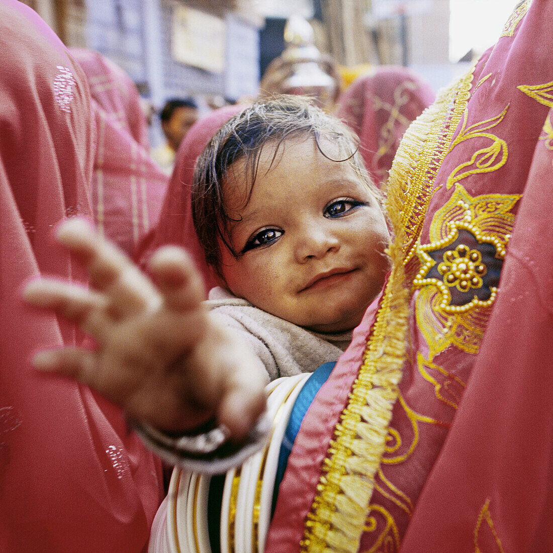Young child is being held by women in colourful sari at a traditional Rajasthan wedding. Child has black make up around eyes This is done from birth to ward off evil eyes This wedding was held in Jodhpur. India.