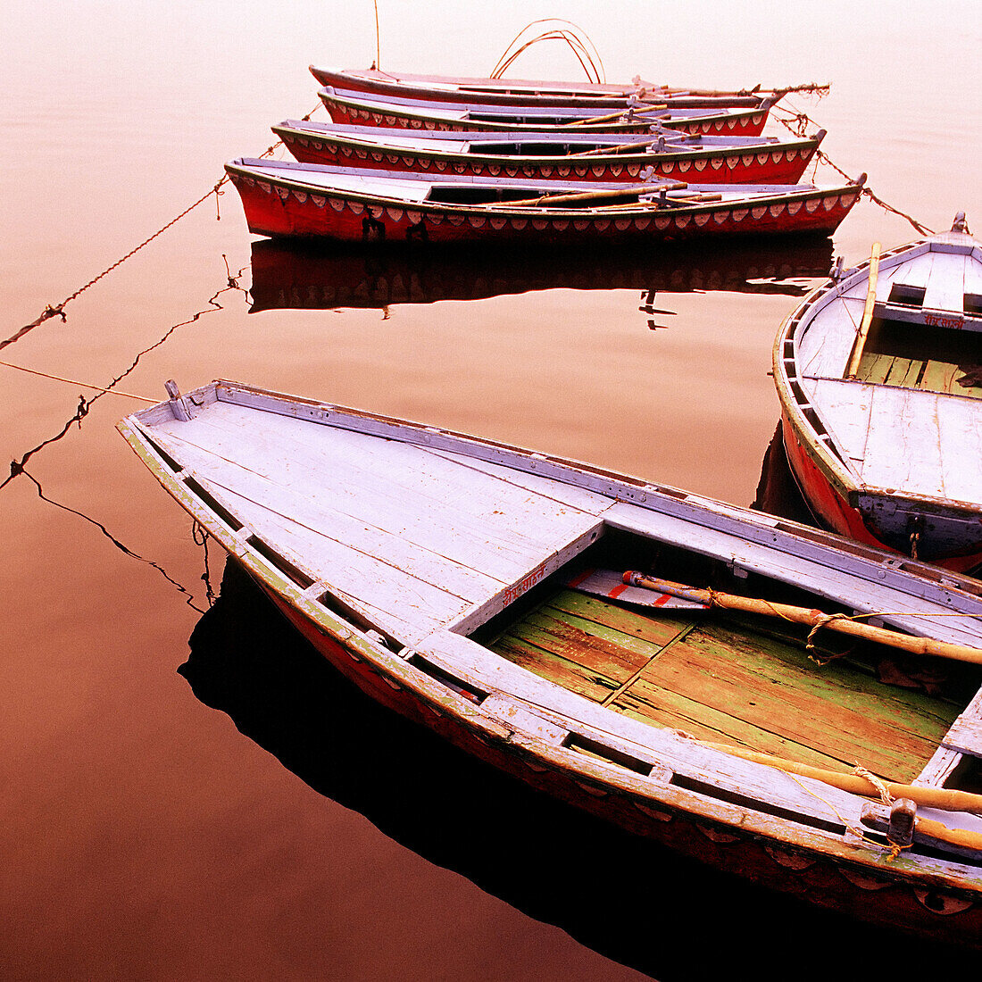 Colourful painted wooden row boat tied up at dusk on the calm water of a lake. India.