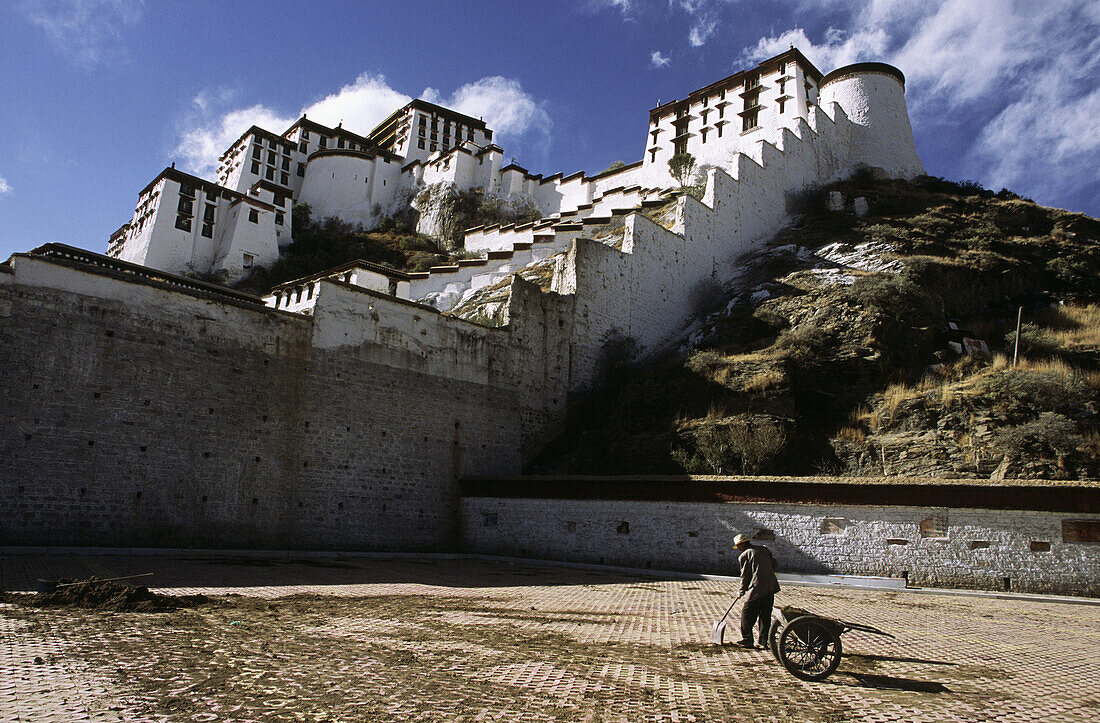 Older male with wheelbarrow fixing the tiled pavement outside of Potala Palace in Lhasa, Tibet. China.