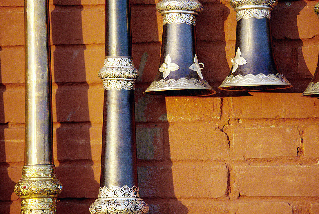 Brass souvenir Tibetan horns hanging on the bright red painted brick wall.