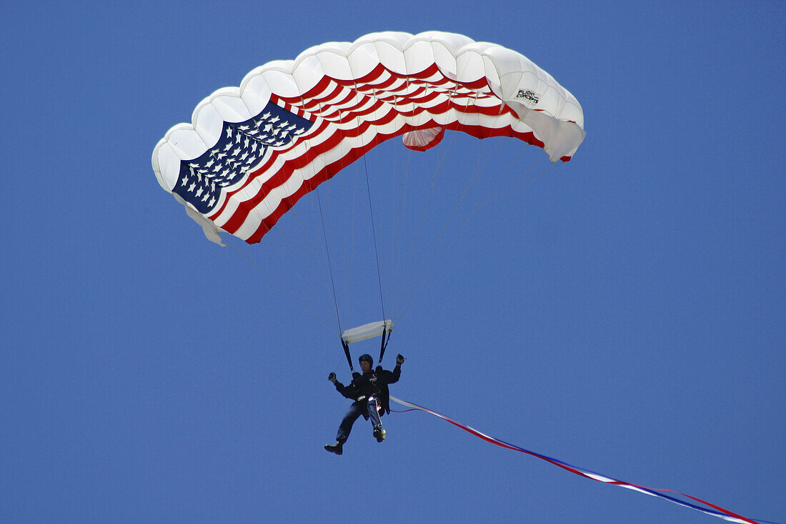 Man parachuting down to the ground with an American flag as a canopy, against a clear blue sky
