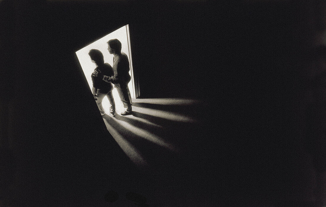 30s 40s man and male adolescent silhouetted in doorway. Bright light in room they are entering; darkness in room they are leaving.