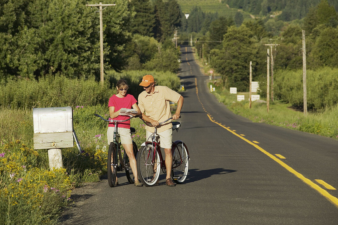 A couple read their mail by a country mailbox while riding their bike in Parkdale, Oregon. USA.