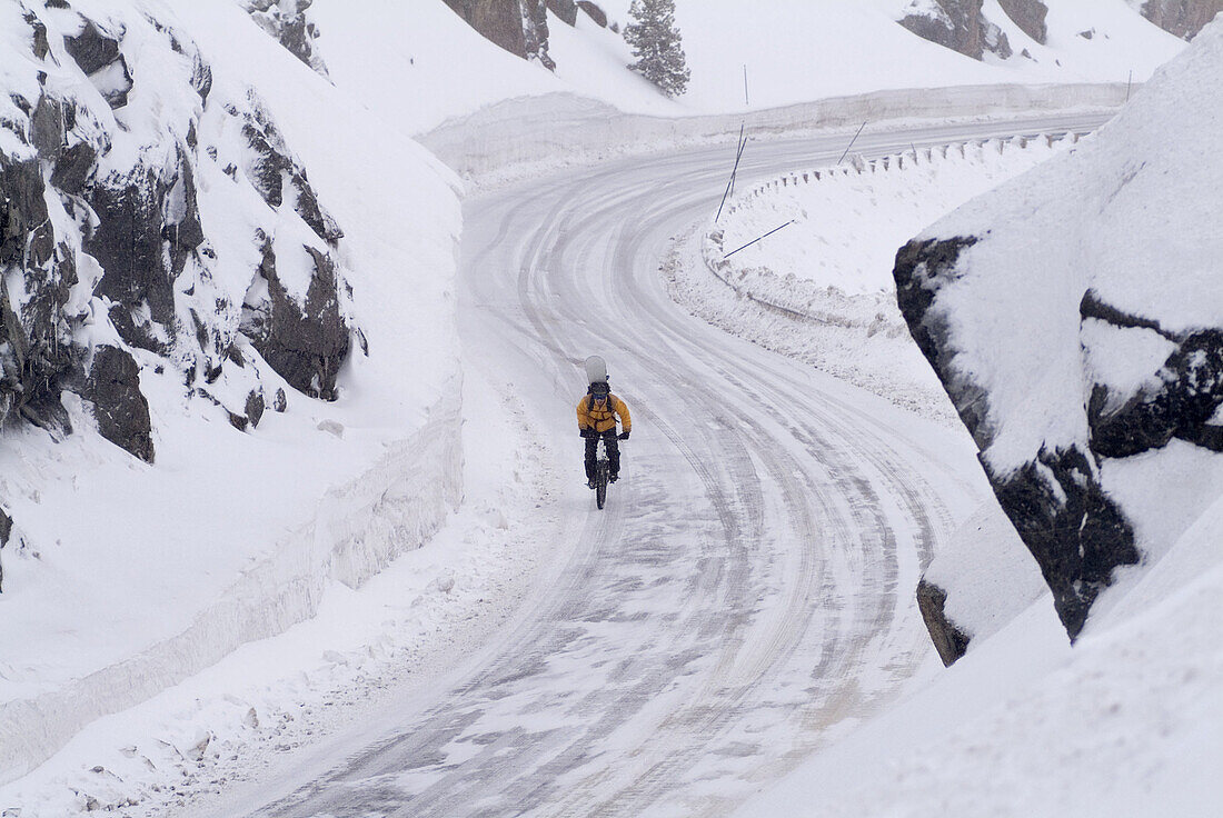Man riding his mountain bike with a snowboard on his back in winter on Donner Summit, California. USA