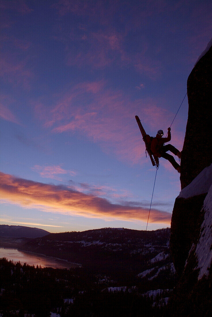 Man rappelling during small avalanche with skis on his back on Donner Summit, California. USA