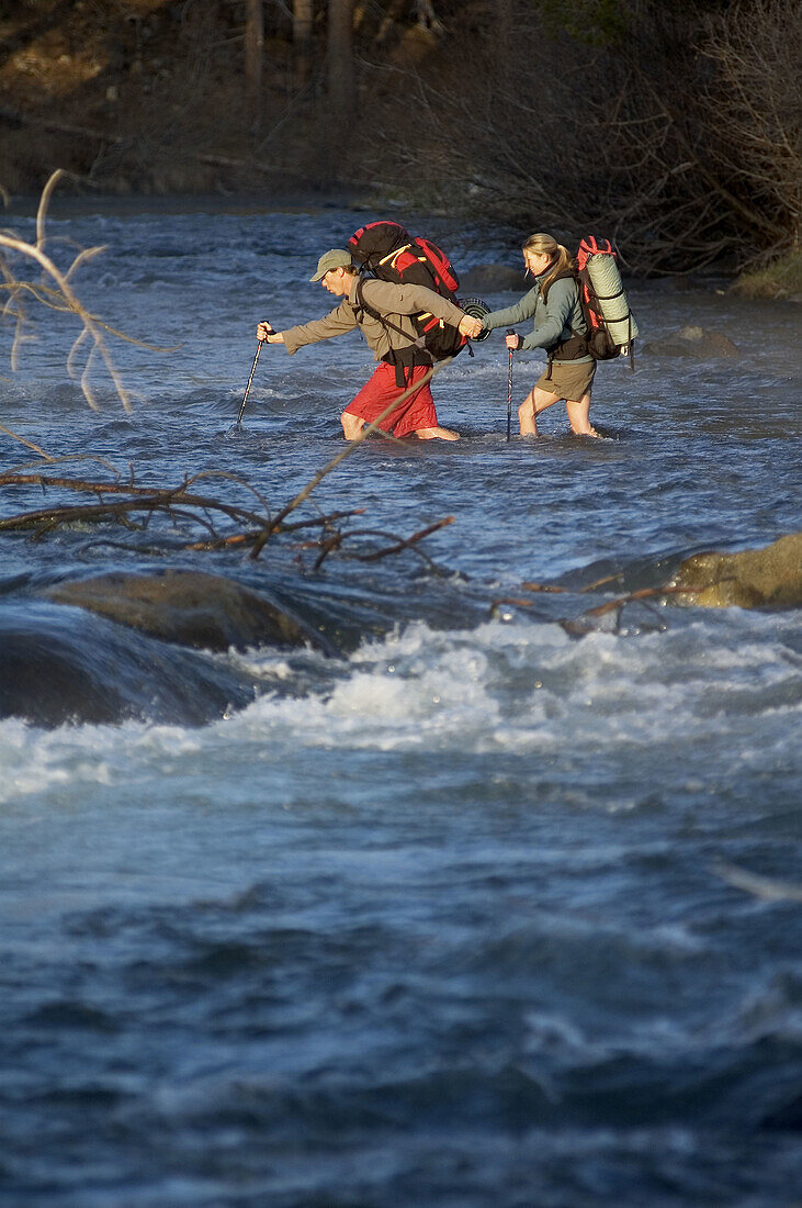 A couple helping each other to cross a river near Truckee, California. USA
