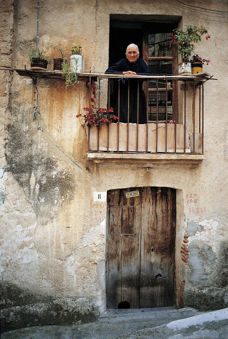 Woman in black looking out from balcony in Sperlinga. Sicily, Italy