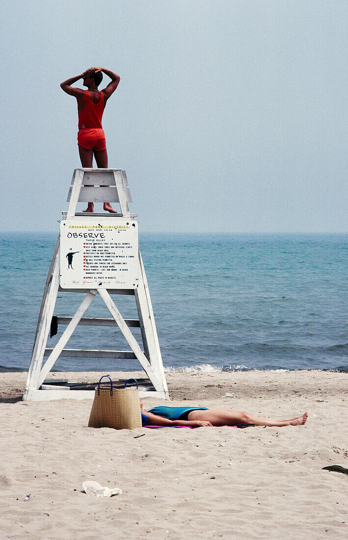 Lifeguard takes a stretch while a beach patron takes a sleep at 56th beach. Chicago. Illinois