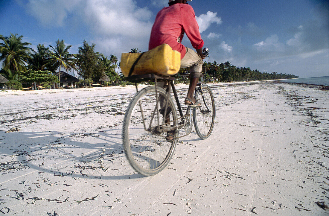Local man riding ancient bicycle along beach, near Bwejuu. Zanzibar. Tanzania. Indian Ocean