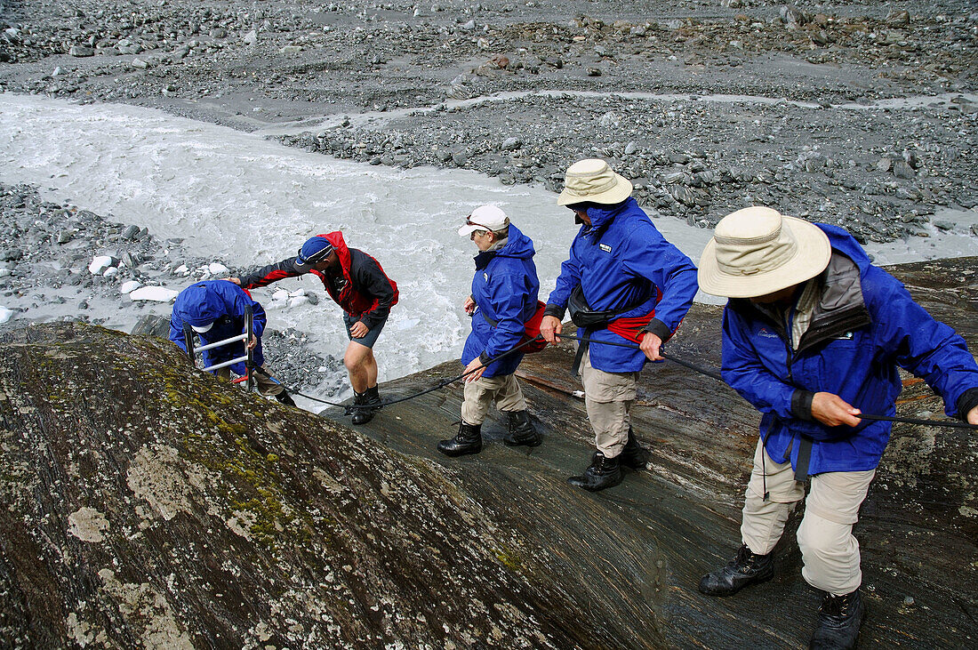 Ecotourists descending from Franz Joseph glacier with help from guide, Westland National Park, New Zealand.
