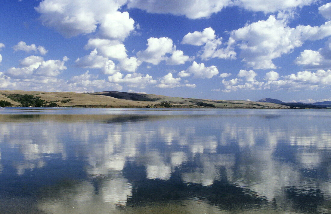 Cumulus clouds and dry hills reflected in Suisun Bay. Extreme east arm of San Francisco Bay. Solano co. (N) and Contra Costa co. (S), connected with San Pablo Bay (W) by Carquinez Strait. Northern California, USA