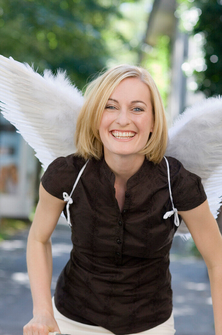 Mid adult woman wearing angel wings riding a bicycle