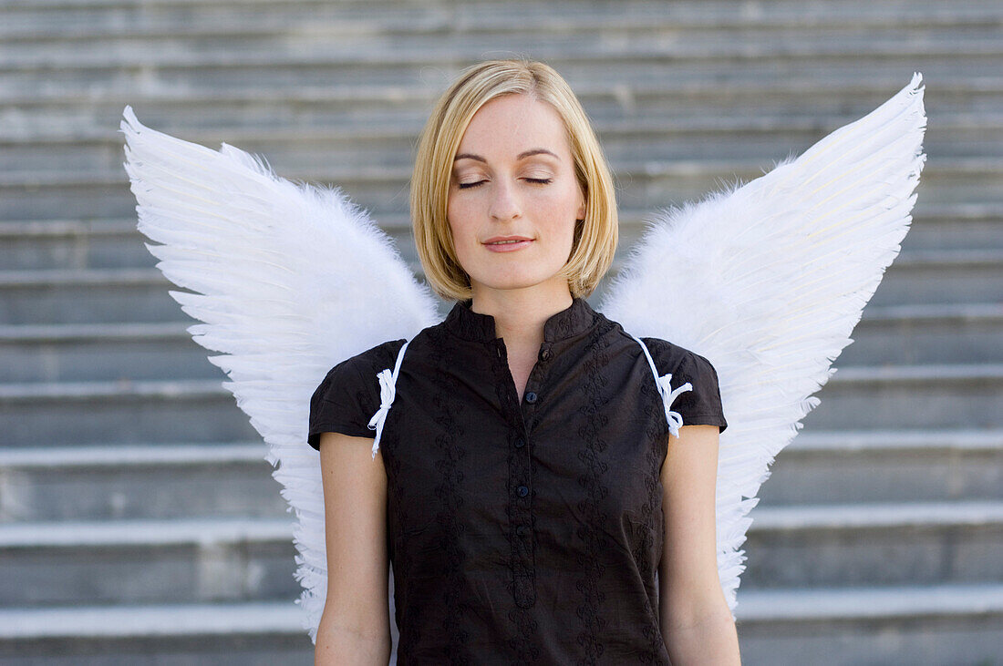 Mid adult woman wearing angel wings with closed eyes