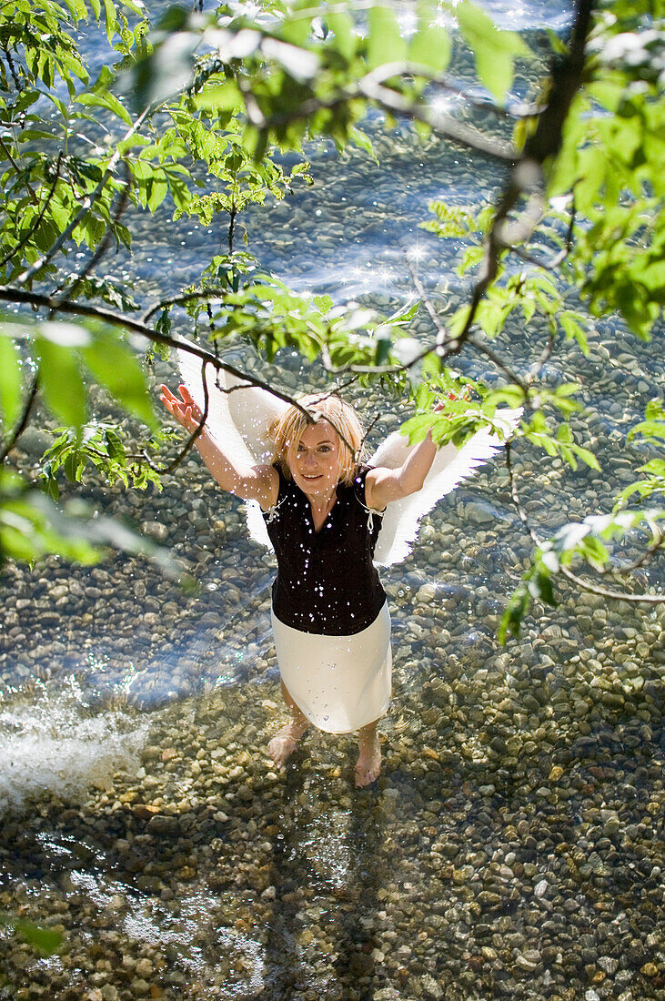 Frau mittleren Alters mit Engelsflügeln steht im Starnberger See, spritzt mit Wasser, Bayer, Deutschland