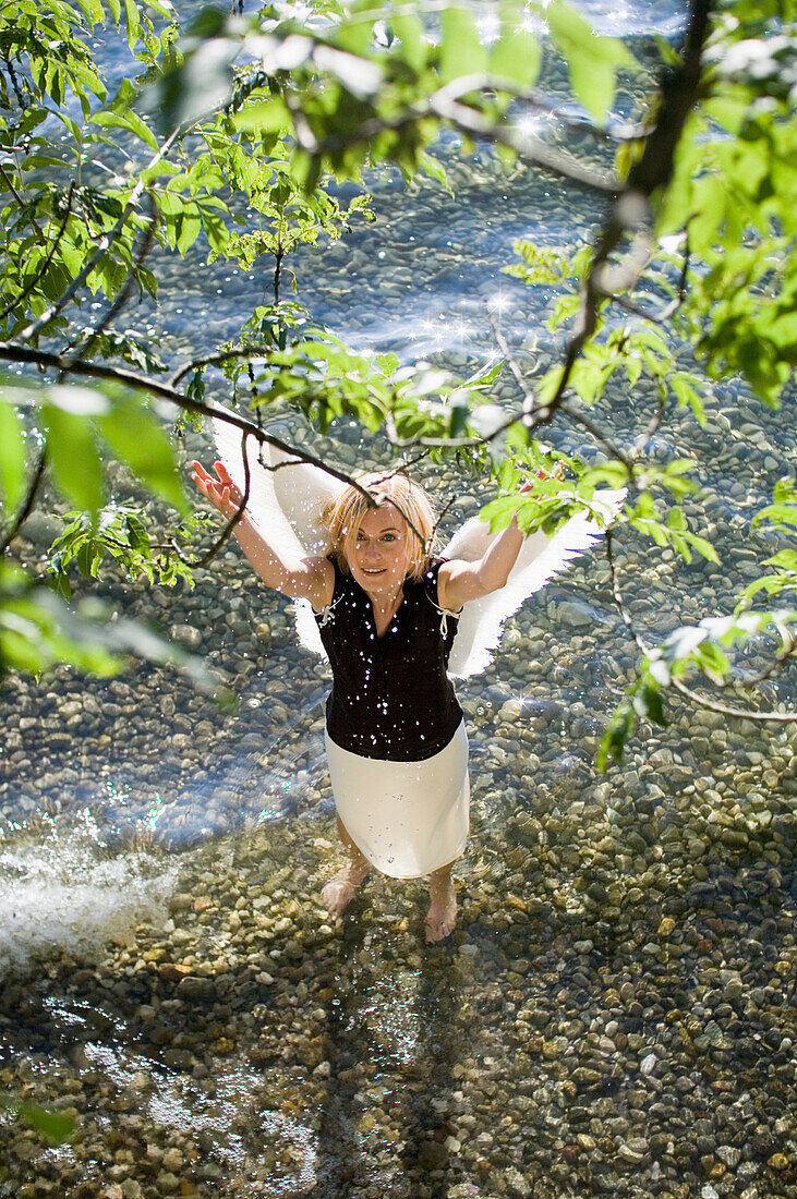 Mid adult woman wearing angel wings standing in lake Starnberg spraying water, Bavaria, Germany