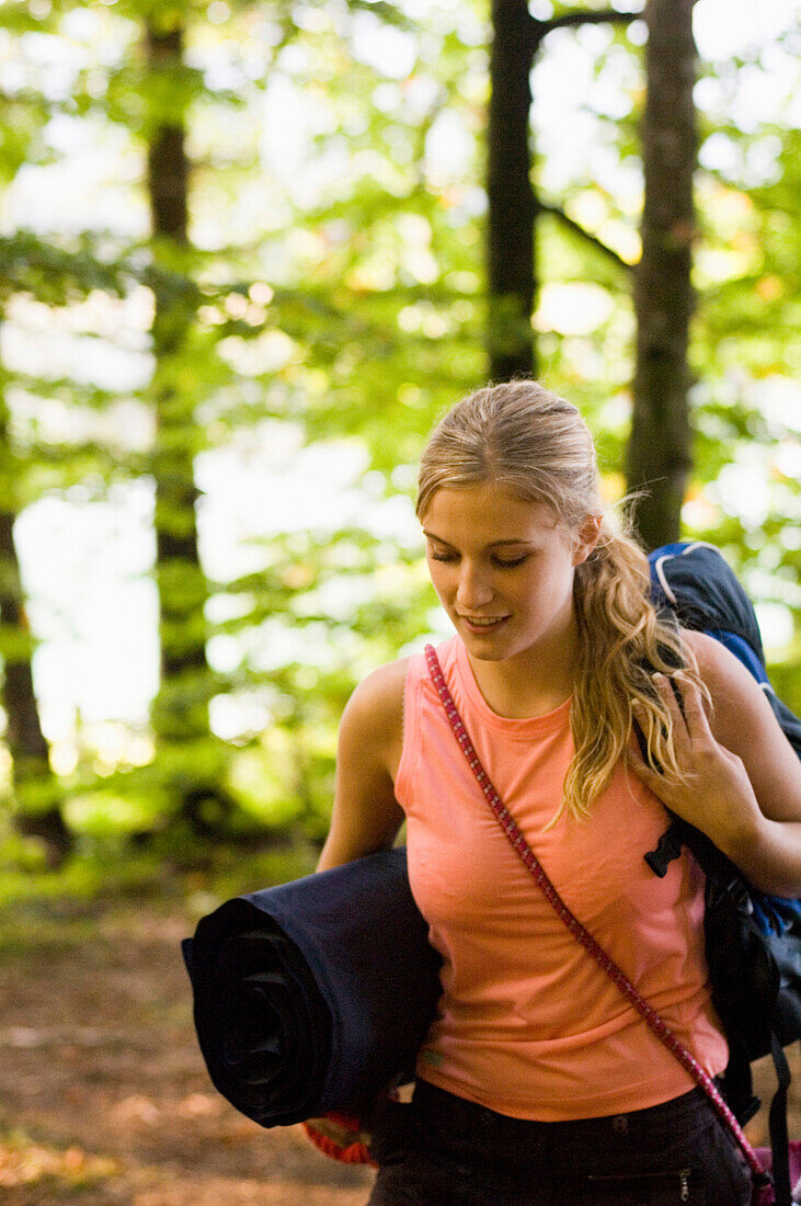 Junge Frau mit Rucksack und Isomatte wandert durch einen Wald