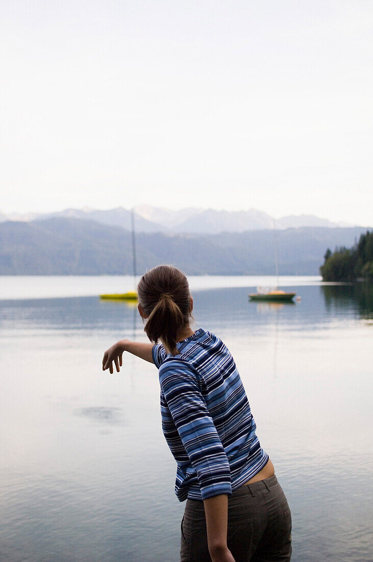 Young woman throwing a stone in lake Walchensee, Bavaria, Germany