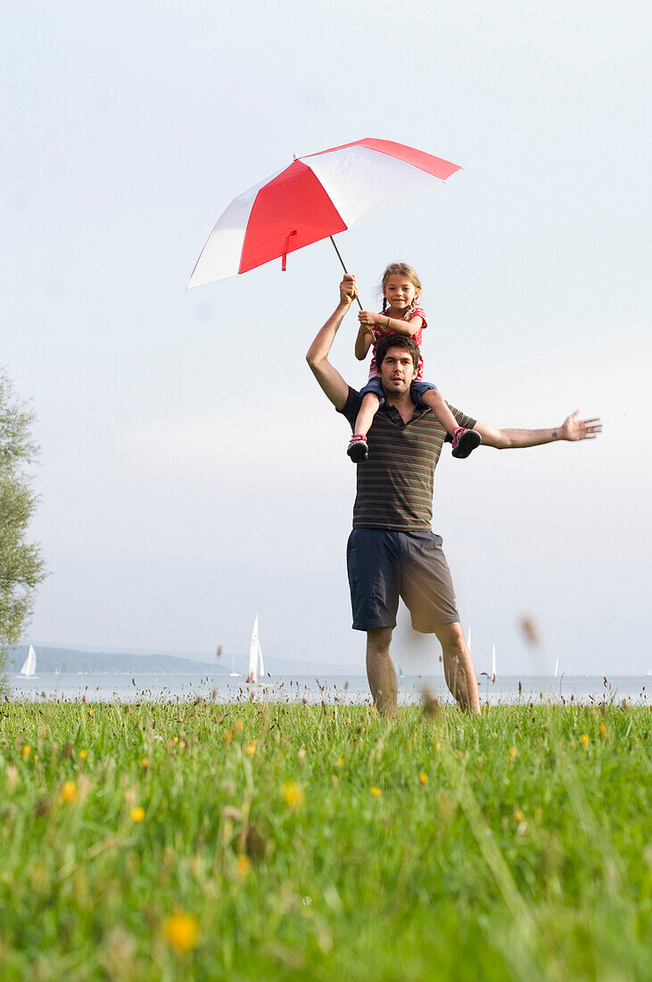 Father giving daughter (4-5 years) a piggyback, girl carrying sunshade, Lake Ammersee, Upper Bavaria, Bavaria, Germany