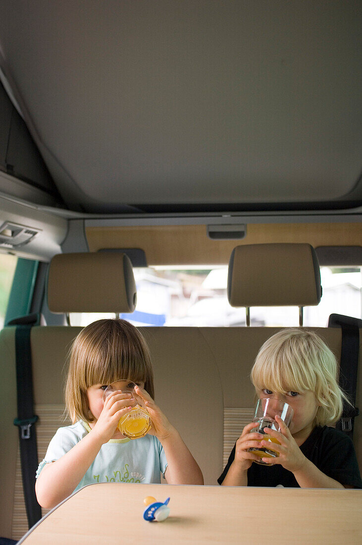 Two children sitting in a camper bus drinking orange juice, Bavaria, Germany