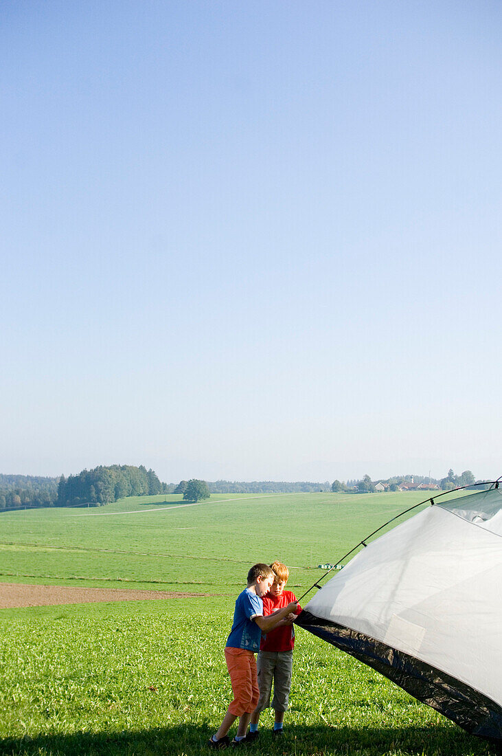 Children putting up a tent in a meadow, Bavaria, Germany