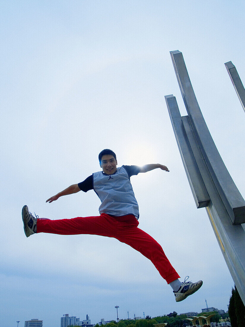 Asian (Chinese) young man straddle jumping facing down to the camera, sky has been blue-saturated