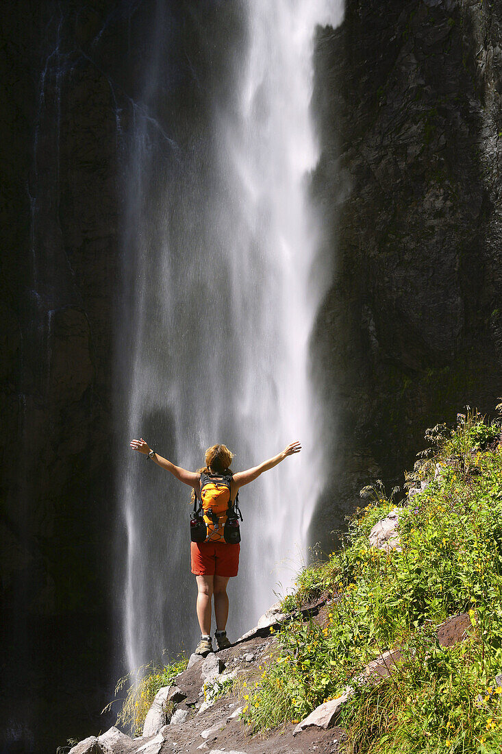 Female hiker basks in the mist of Comet Falls along trail to Van Trump Park in Mt. Rainier National Park, Washington, USA