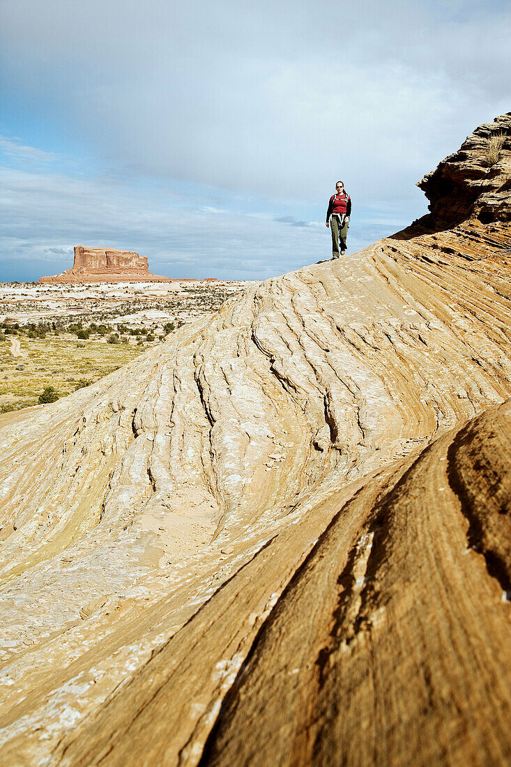 Female hiker on sandstone slickrock with Merrimac Butte in the background near Canyonlands National Park, Utah, USA.