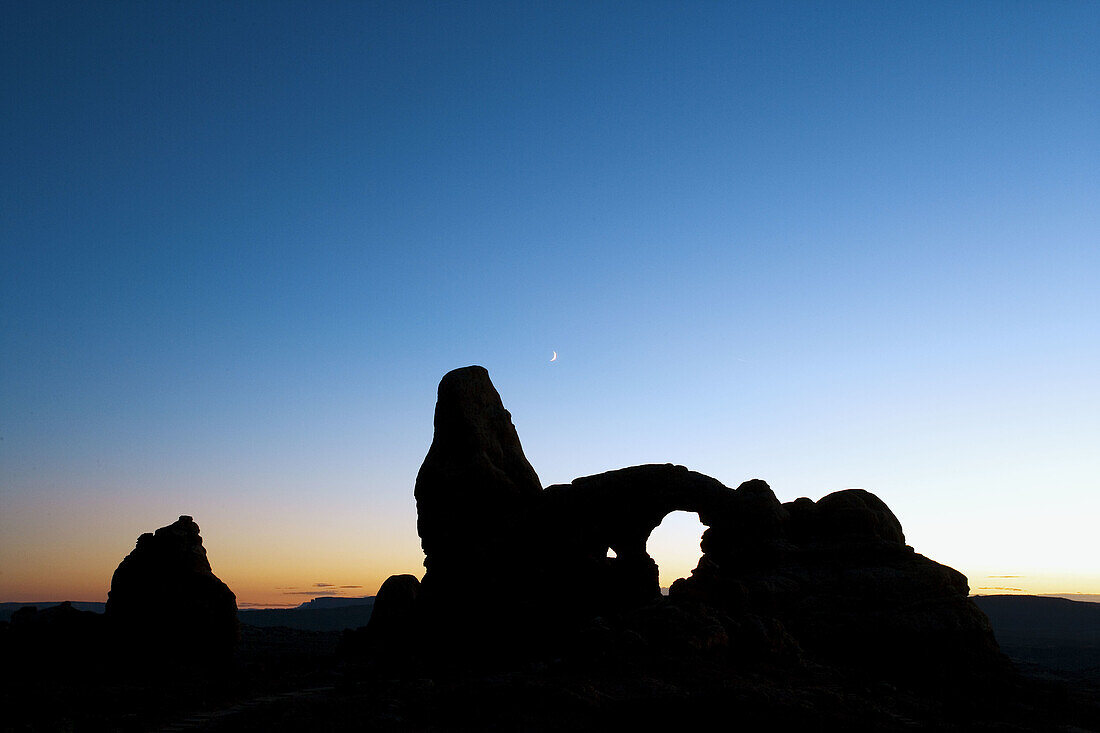 Turret Arch and a sliver of moon against a deep blue sky after sunset, Arches National Park, Utah, USA.