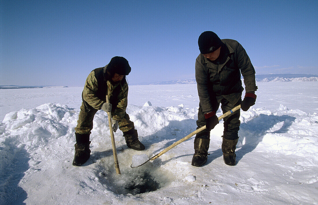 Fishermen digging ice hole on frozen Baikal lake in winter to recover their net, Siberia, Russia