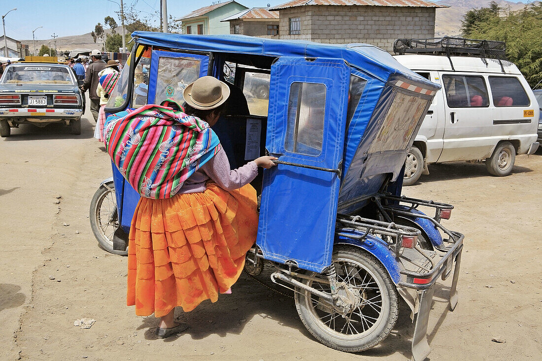 Indian woman entering a motorized taxi. Desaguadero, Peru.