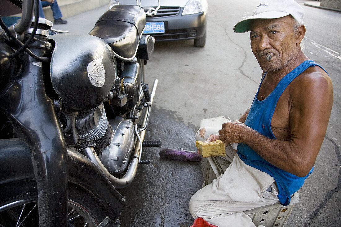 Man smoking cigar and repairing his motorbike. Havana, Cuba