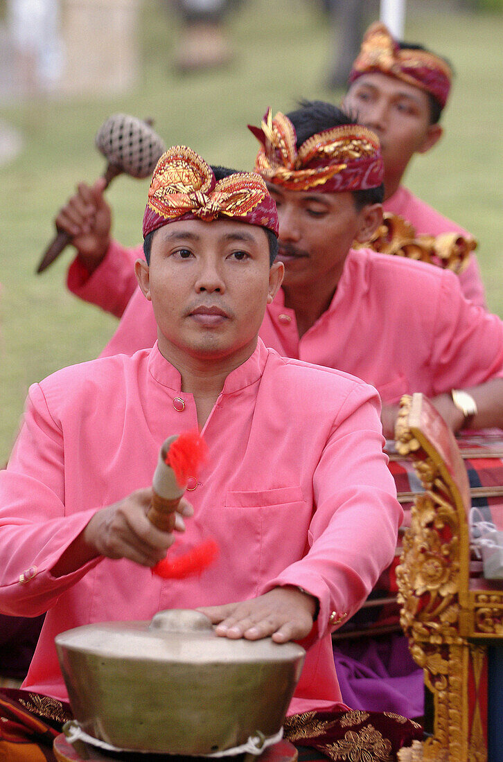 three balinese musicians playing gamelan