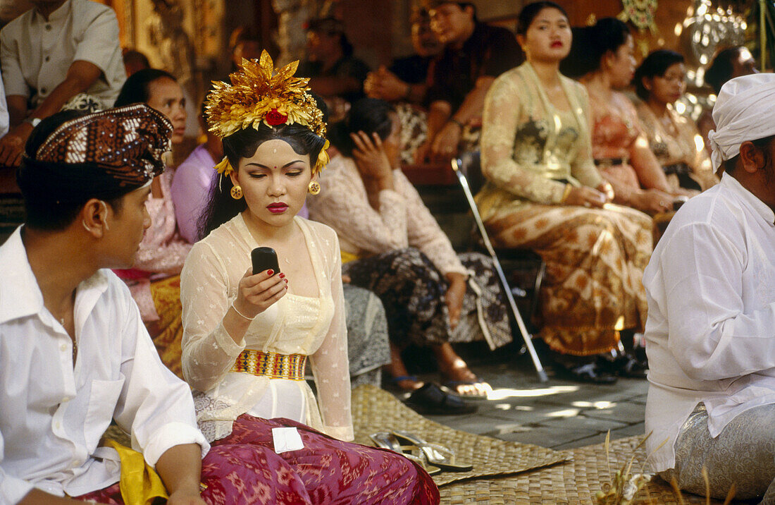A bride checks her mobile phone during a modern Balinese wedding reception. Ubud. Bali. Indonesia.