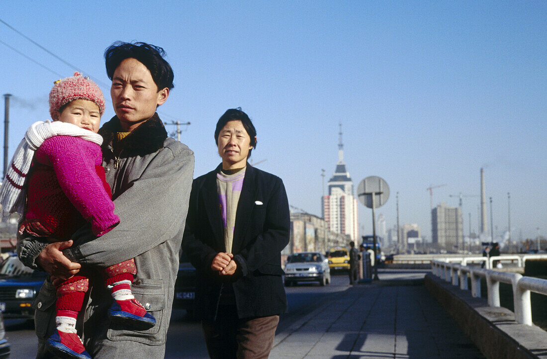 A family walk along a road outside the Beijing railway station. Beijing. China.