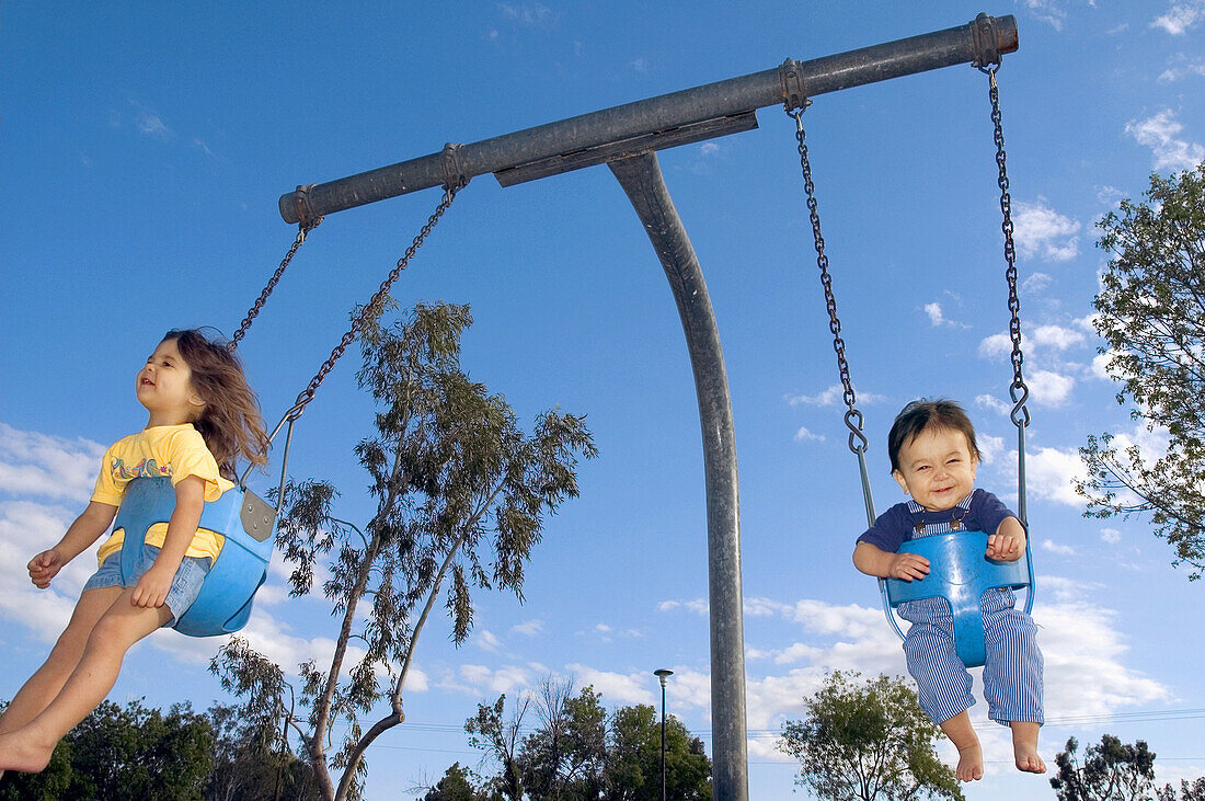 2 year old girl and 10 month old baby playing in swing at public park, Mesa. Arizona USA