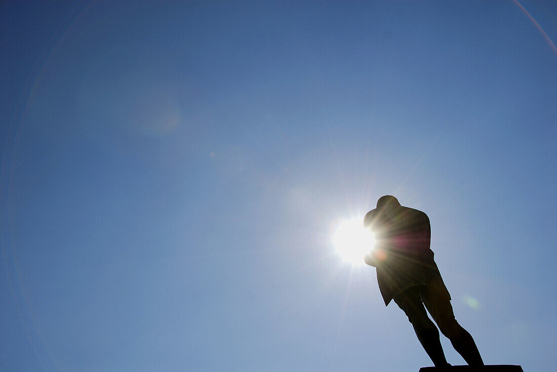 statue of man arms folded with sun peeking through