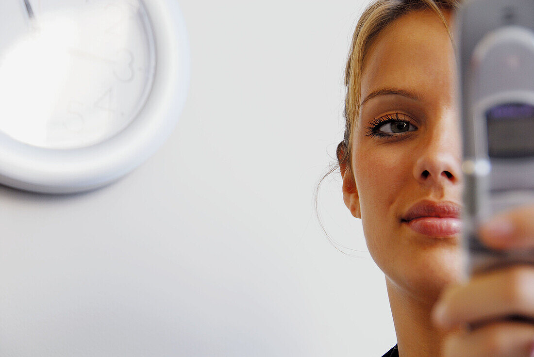 20 yr old woman holding cell phone in office/home with clock on wall