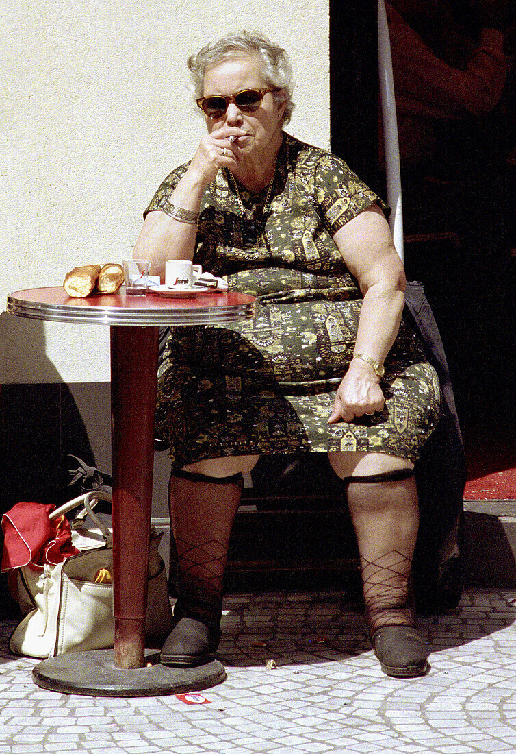Robust woman at table outside cafe, drinking coffee, with knee highs showing