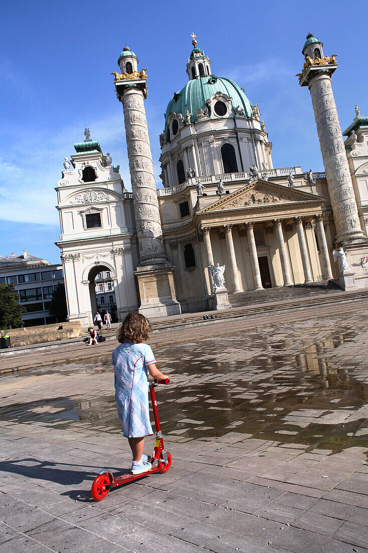 Girl with kick scooter on Karlsplatz with Karlskirche in background, Vienna, Austria