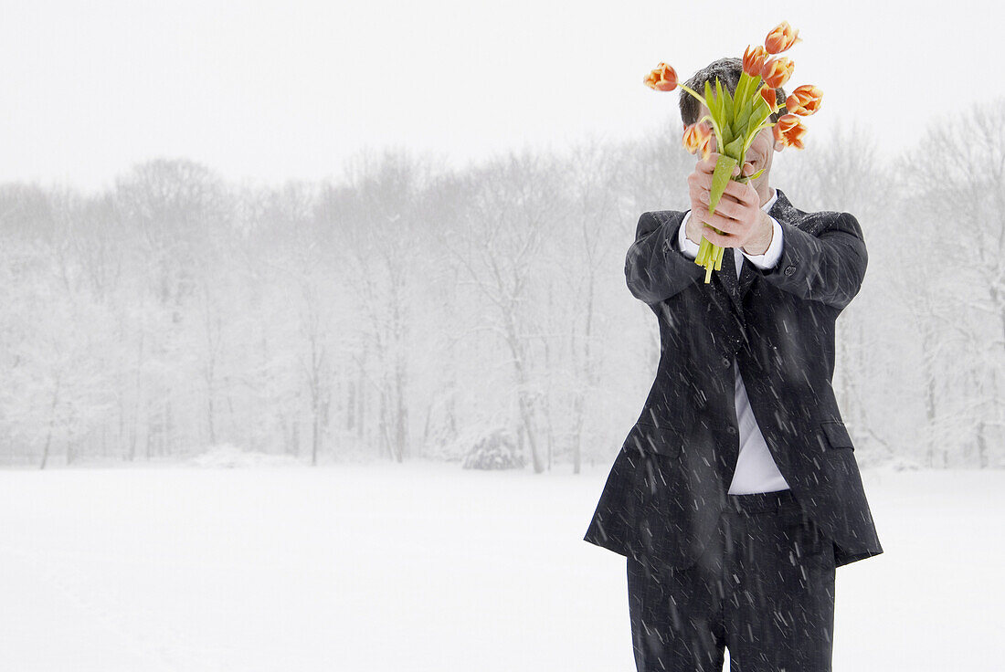 Young man holding a bunch of tulips standing in snow flurry, Munich, Bavaria, Germany