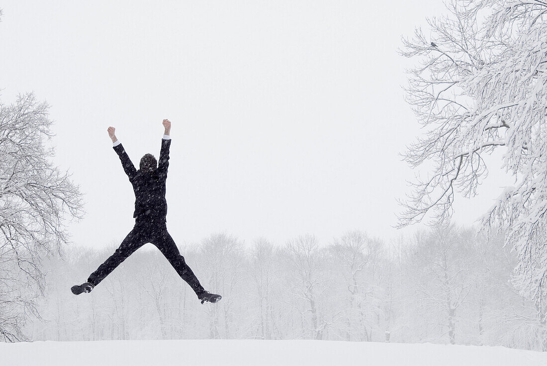 Junger Mann macht Luftsprung im Schneegestöber, München, Bayern, Deutschland