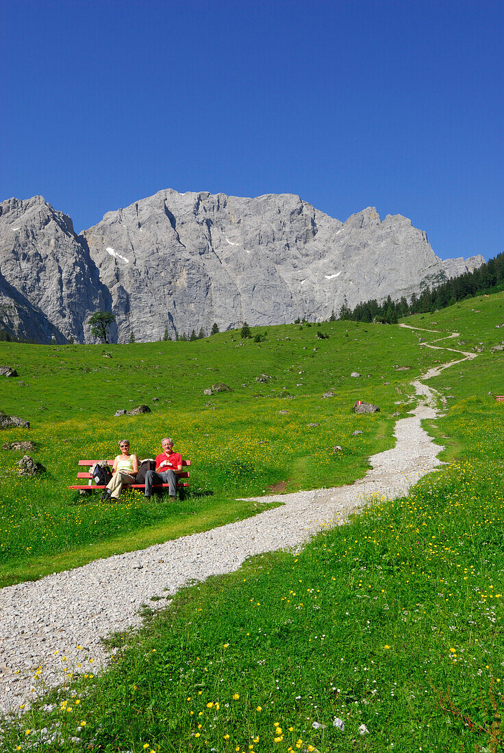 Weg in Almwiese auf Bergkulisse zu mit älterem Paar auf Bank, Eng, Enger Alm, Karwendel, Tirol, Österreich