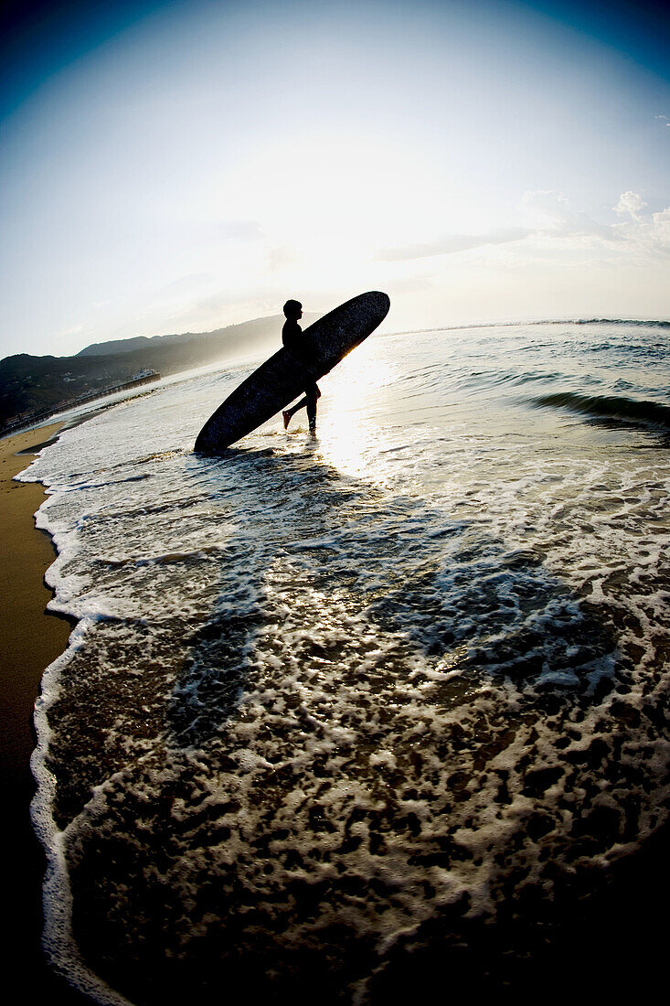 Silhouette of a surfer entering the water at sunrise