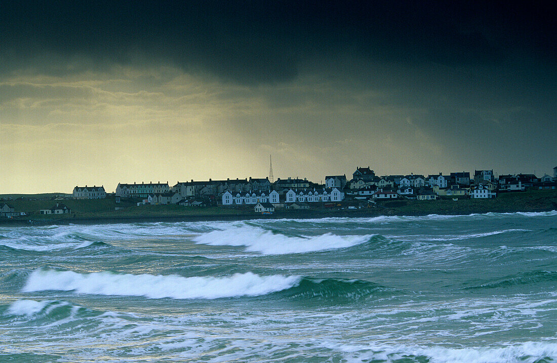 Surge and houses on shore under dark clouds, Portrush, County Antrim, Ireland, Europe