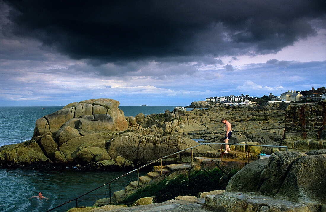 Menschen baden im Meer unter dunklen Wolken, Sandy Cove, County Dublin, Irland, Europa