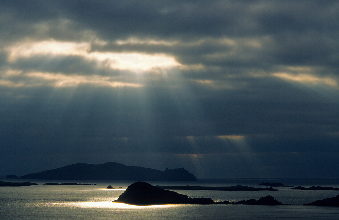 Sonnenstrahlen scheinen durch eine dunkle Wolkendecke über Blasket Island, County Kerry, Irland, Europa