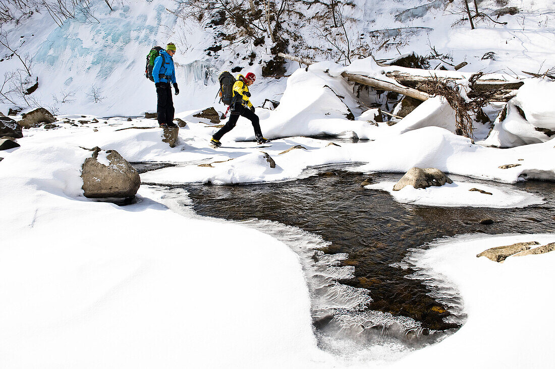 Two men crossing a stream in winter, Hokkaido, Japan, Asia