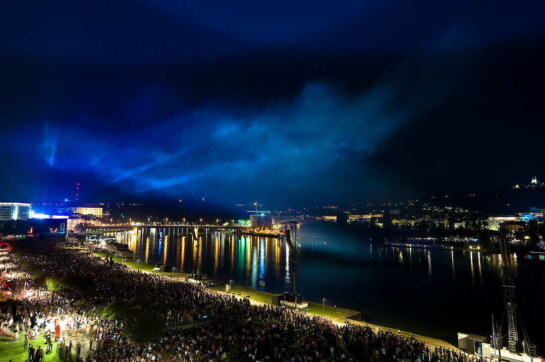 Eine Menschenmenge nachts bei einem Freiluftkonzert an der Donau, Linz, Oberösterreich, Österreich