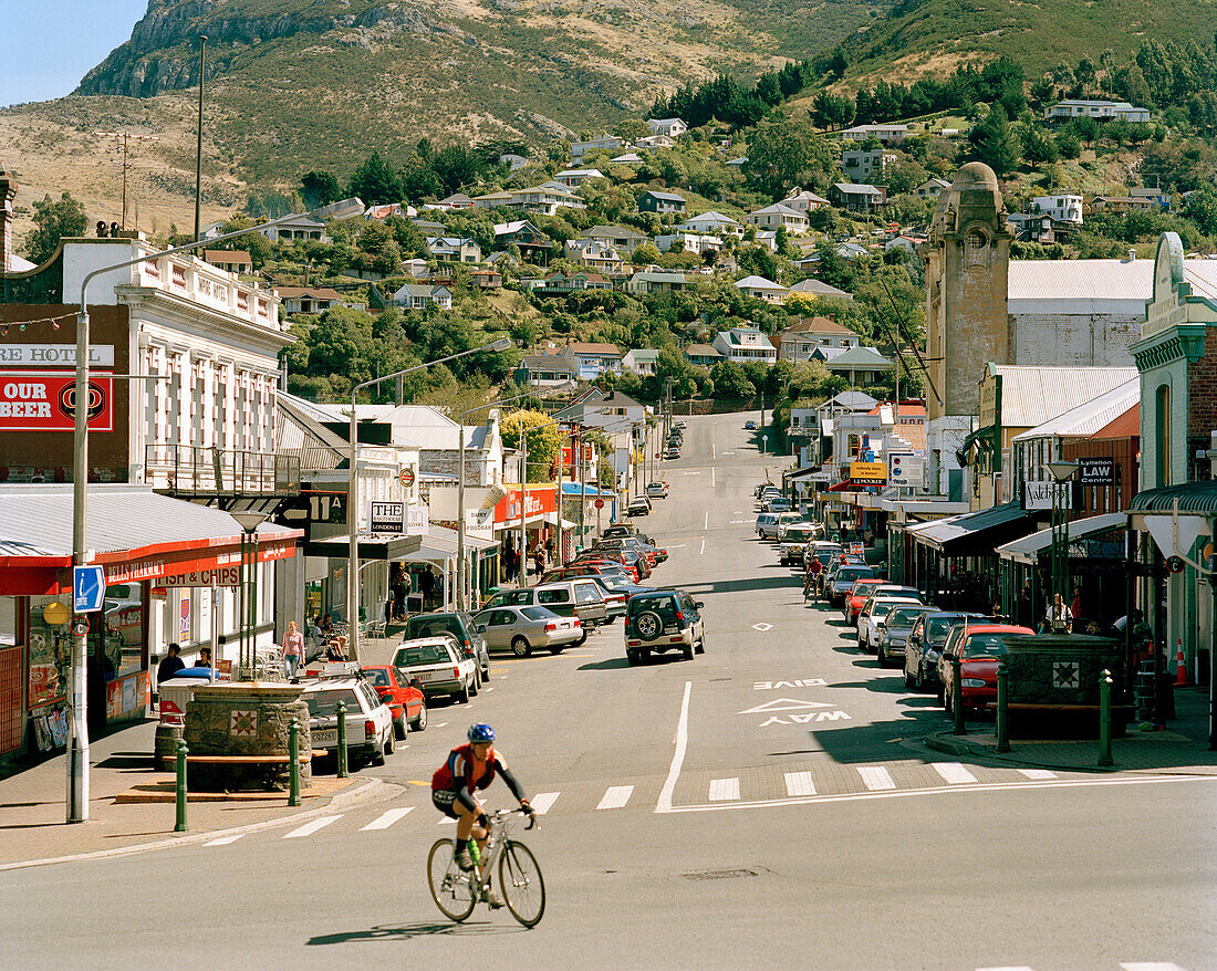 Fahrradfahrer auf der Hauptstraße in Lyttelton im Sonnenlicht, Südinsel, Neuseeland