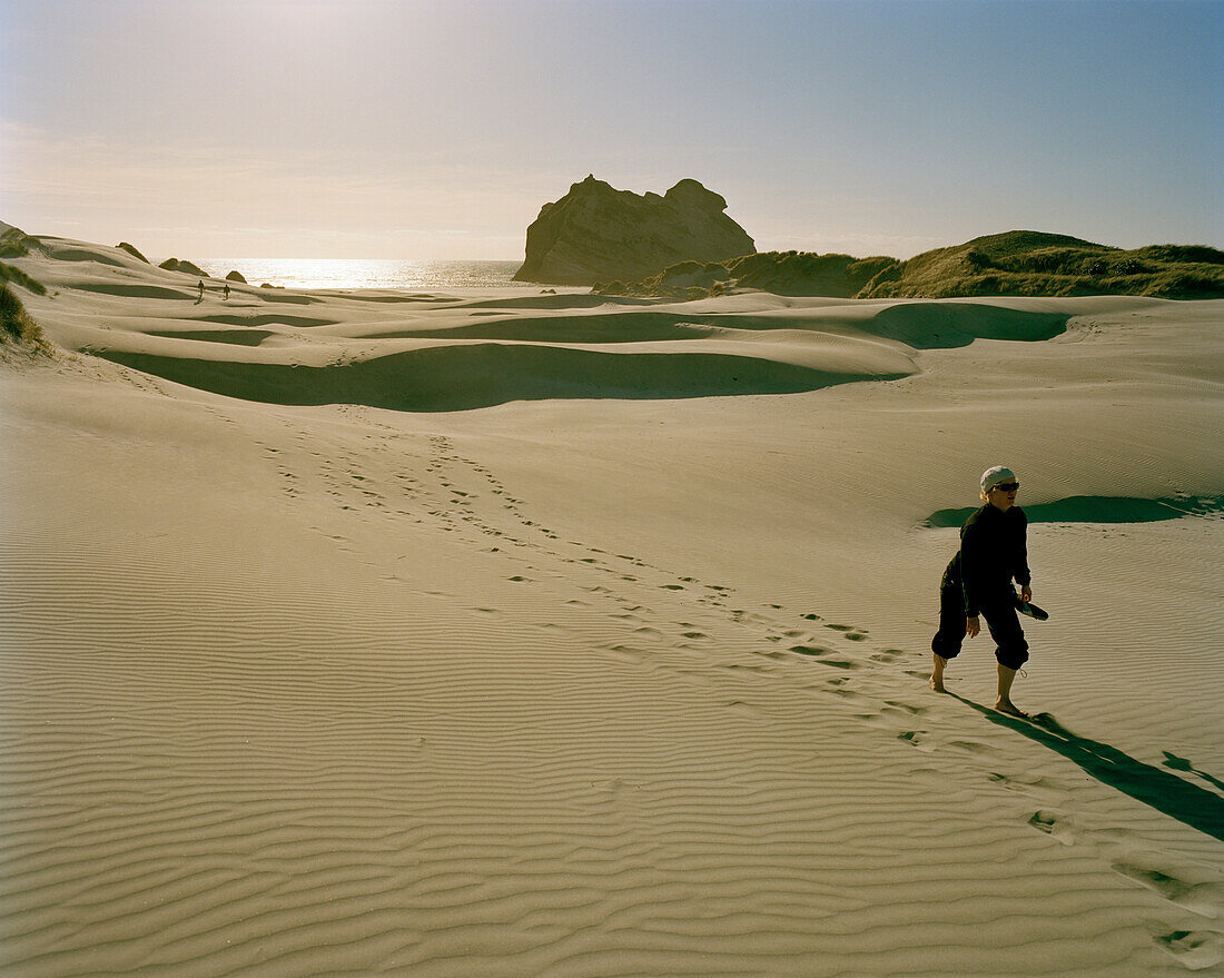 Woman walking through wandering dunes in the sunlight, Wharariki Beach, Northwest coast, South Island, New Zealand